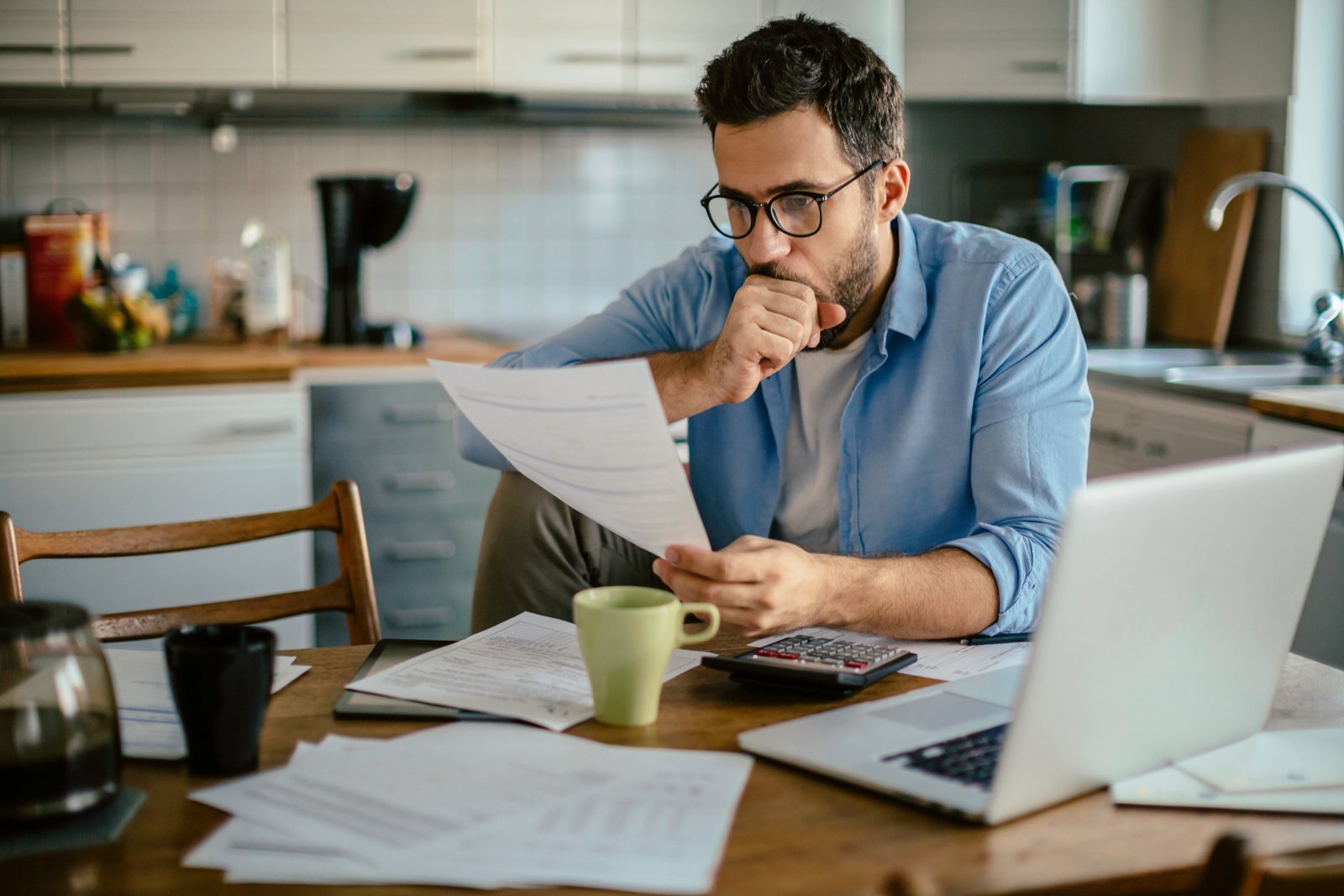 A person reviewing debt statements with a calculator and laptop, ordering balances by interest rate