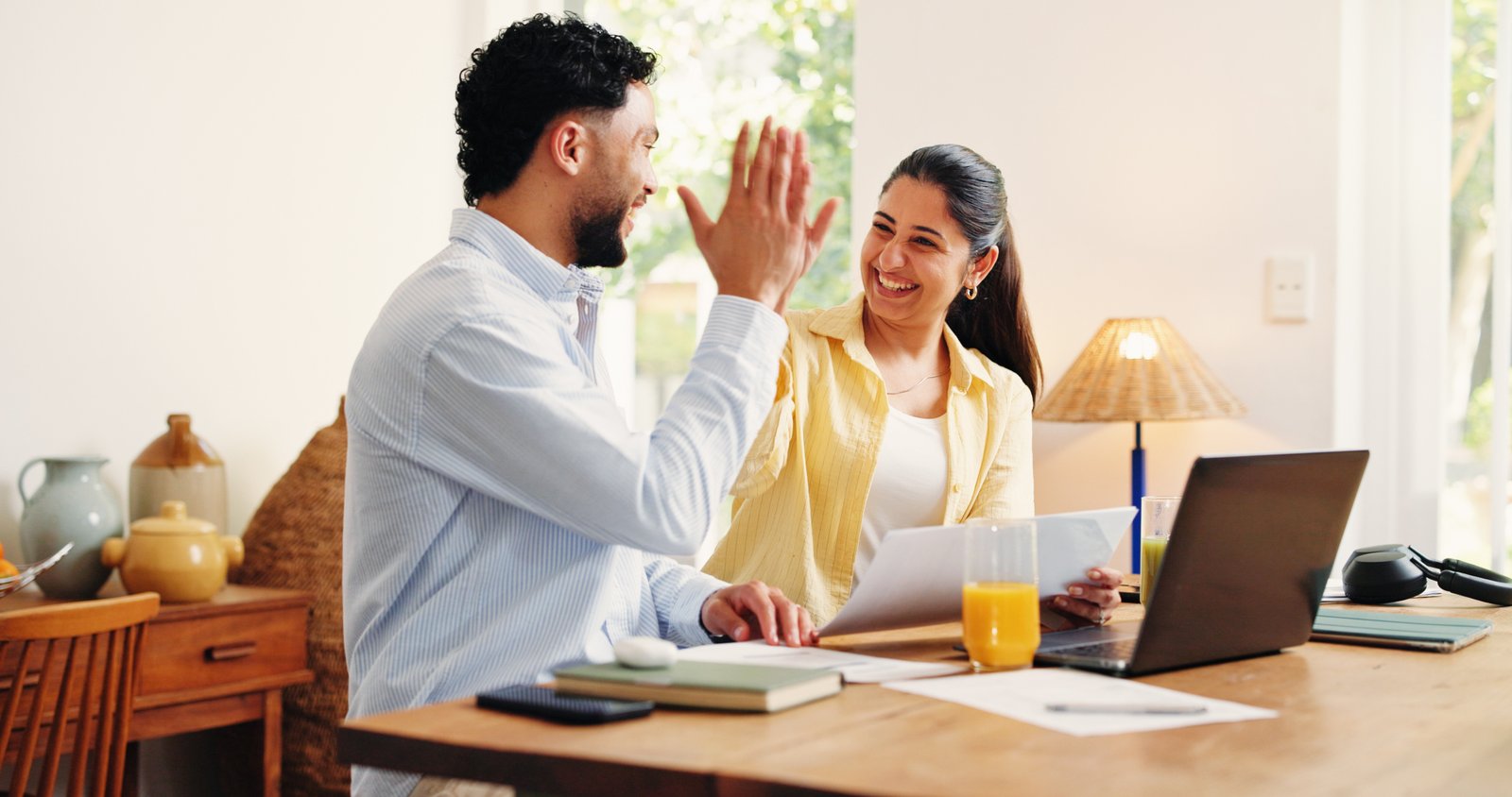 A couple celebrating with a high five while reviewing their finances and debt payoff plan at home